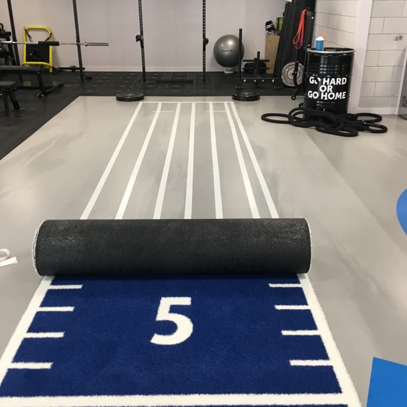 Roll-format training surface being positioned over a marked gym lane